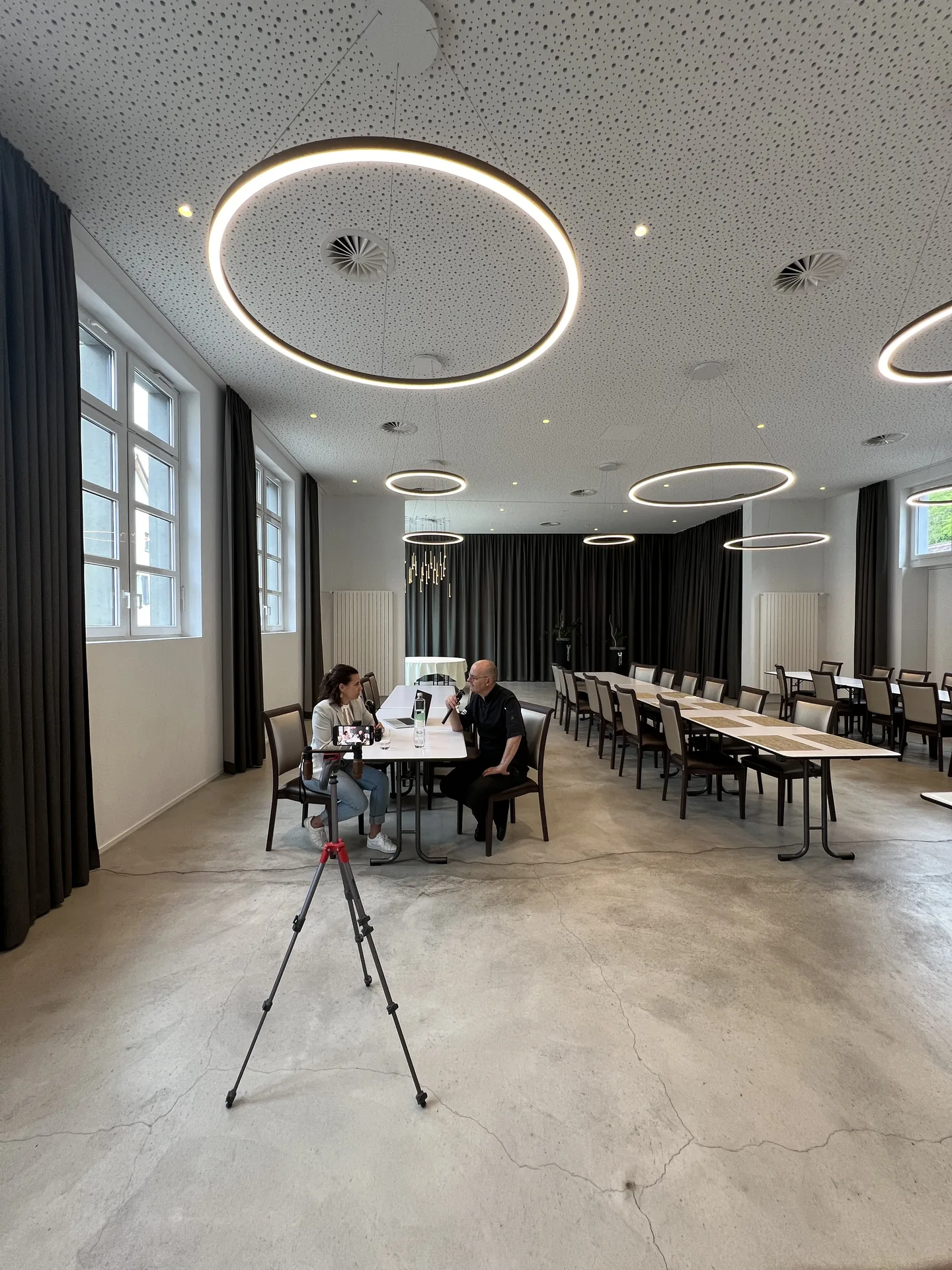 Weitwinkel-Blick auf das Setup des Podcast-Drehs in einem Saal mit Ringleuchten