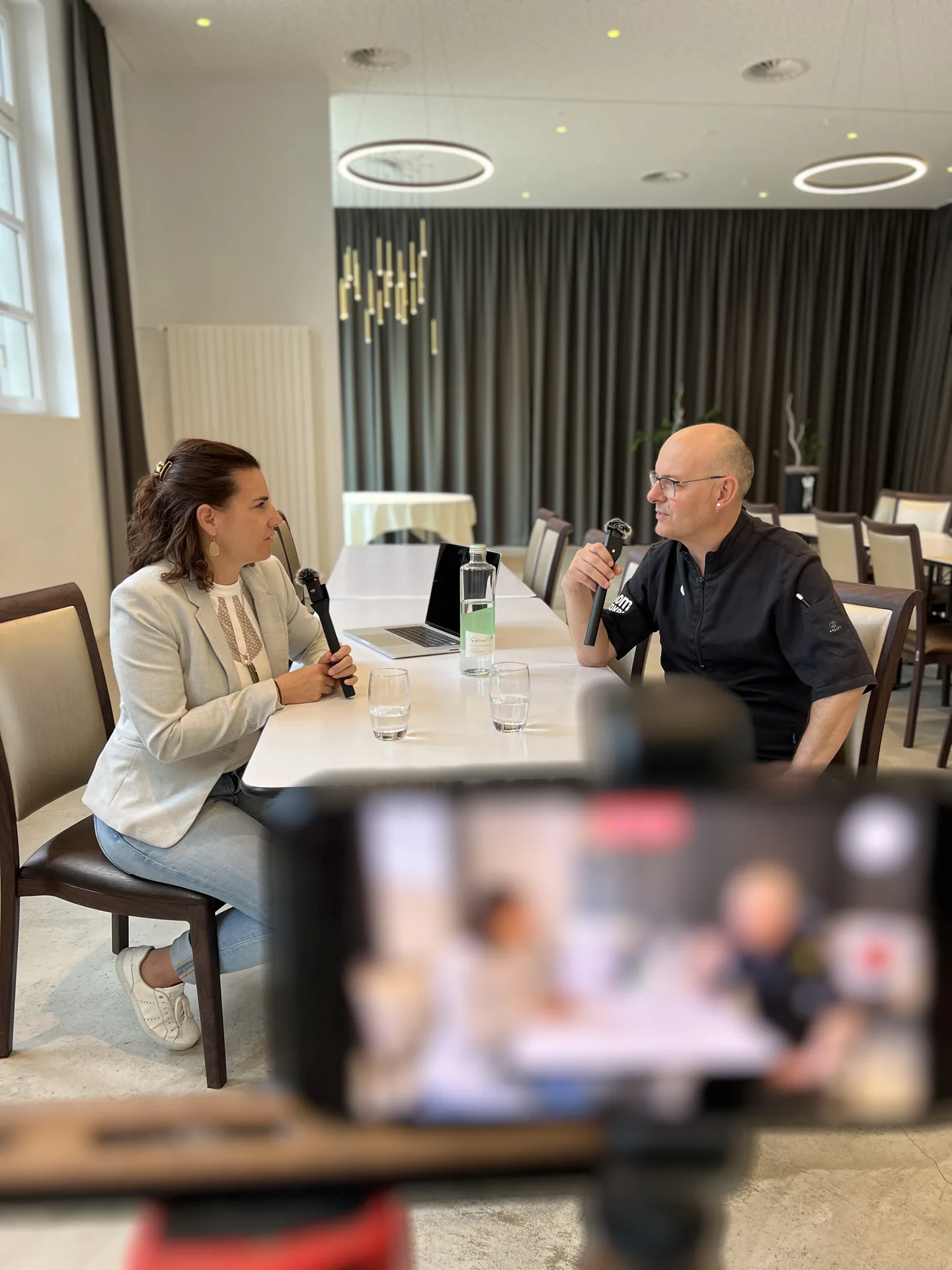 Podcast-Dreh im Saal: Interview-Setup mit zwei Mikrofonen und Kamera im Vordergrund